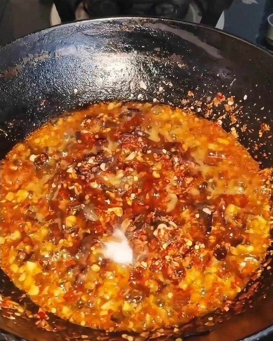 Condimento liquido scuro versato in un wok sfrigolante pieno di carne, peperoncino e aromi.