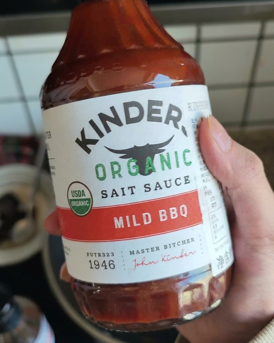 Una mano che tiene una bottiglia di salsa BBQ delicata, pronta per essere versata sul maiale sfilacciato.