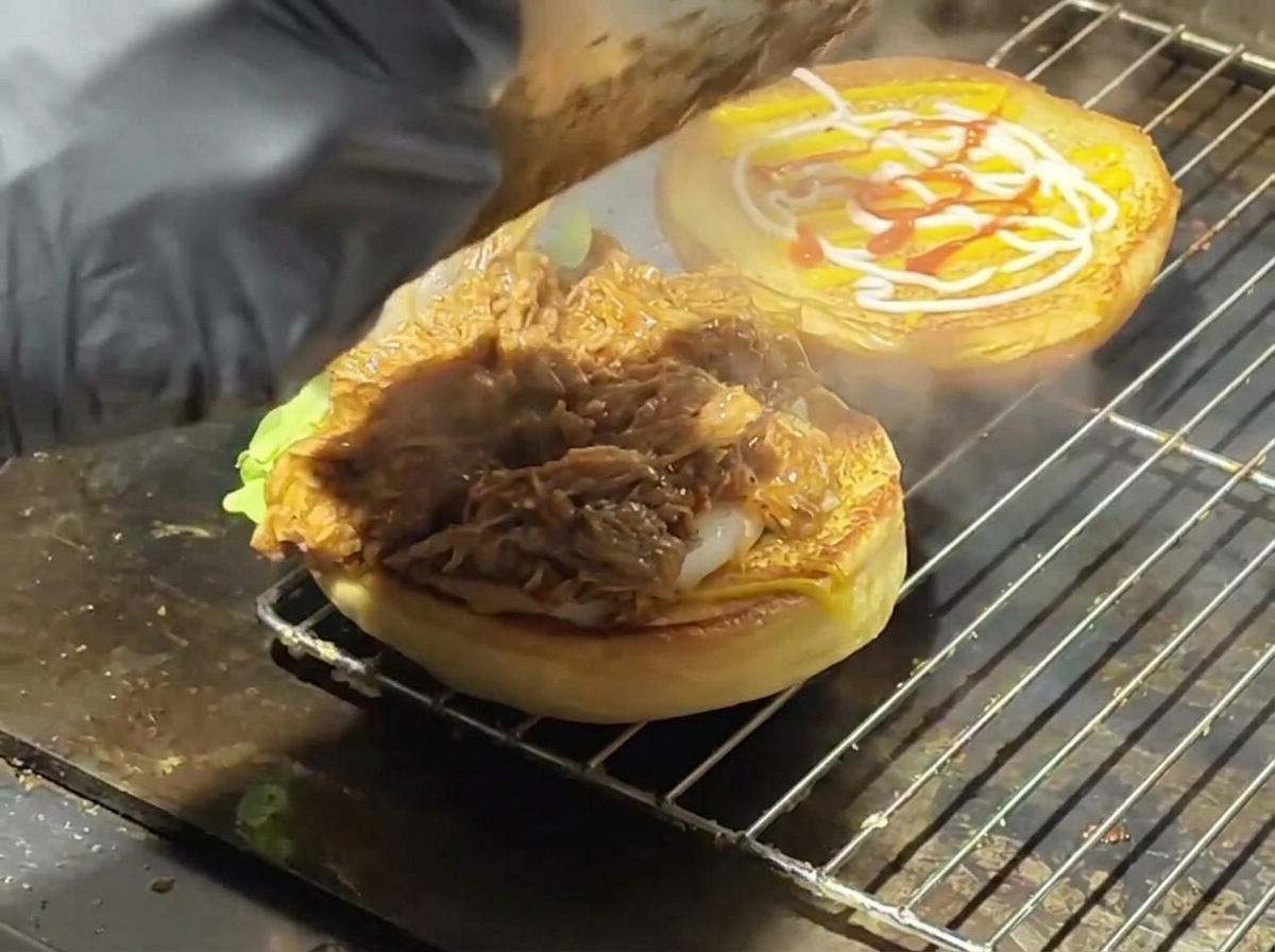Pulled pork succoso servito su un panino tostato con lattuga su una piastra calda.