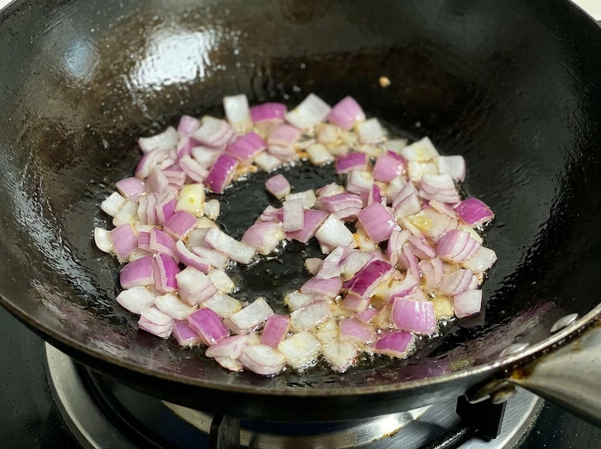 Cipolla rossa tritata che soffrigge in un wok con olio, mescolata da una spatola nera.
