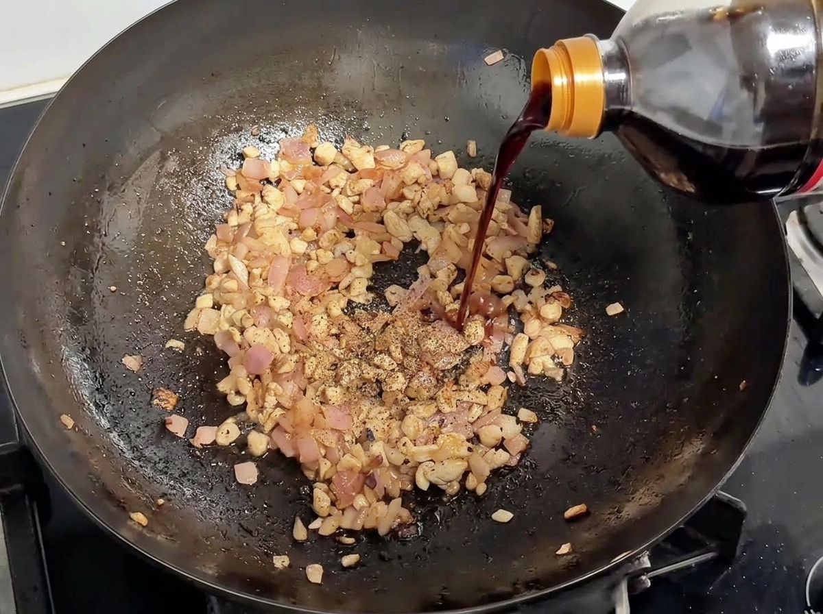 Salsa di soia versata da una bottiglia nel wok con carne rosolata e cipolla, con pepe nero.