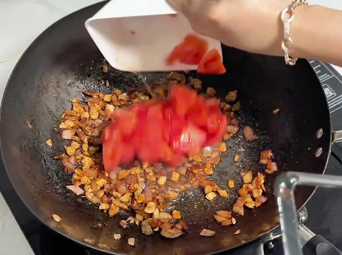 Pomodori rossi freschi tritati aggiunti in un wok con carne rosolata.