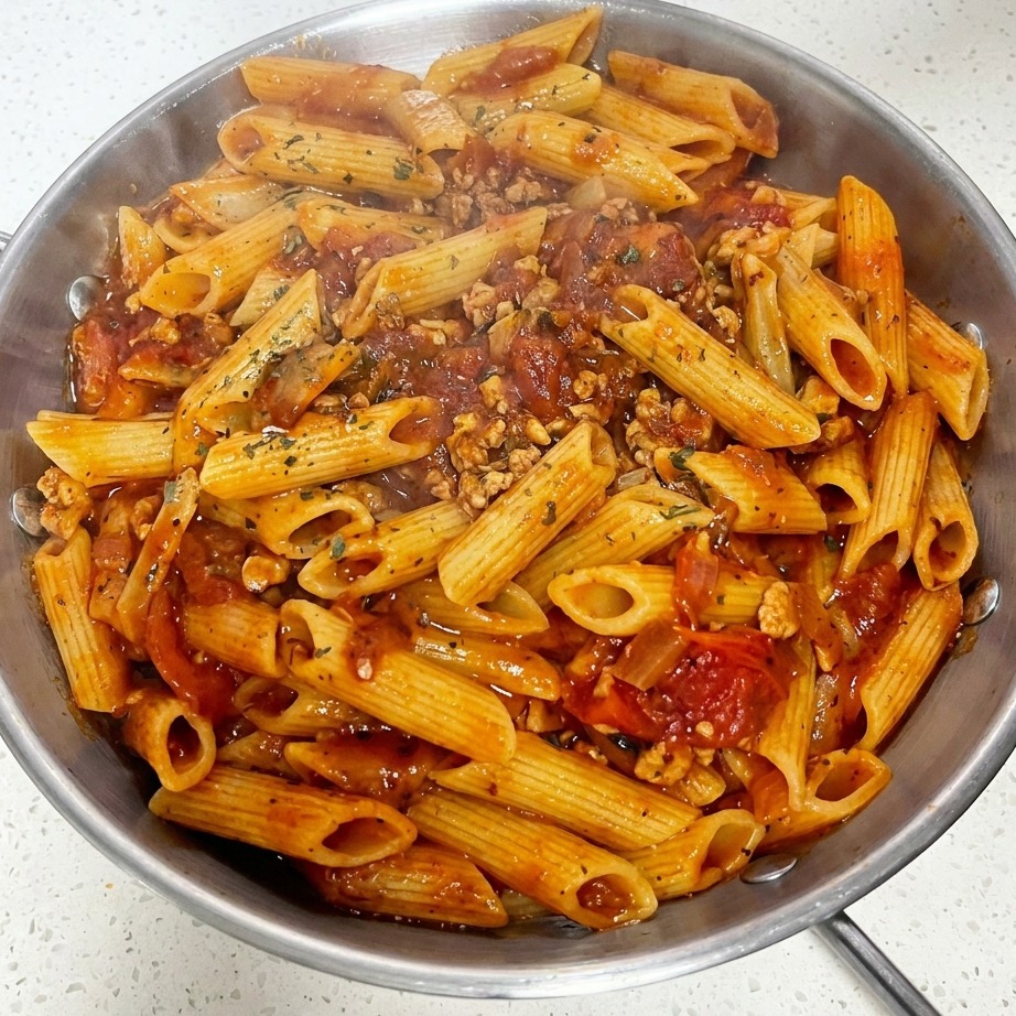 Primo piano di una padella con pasta al sugo di carne, formaggio fuso e prezzemolo secco spolverato sopra.