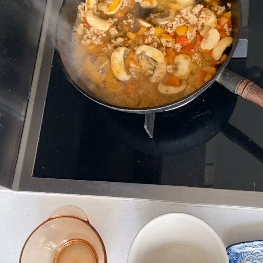 Un sugo di carne, funghi e pomodori che sobbolle in una padella nera.