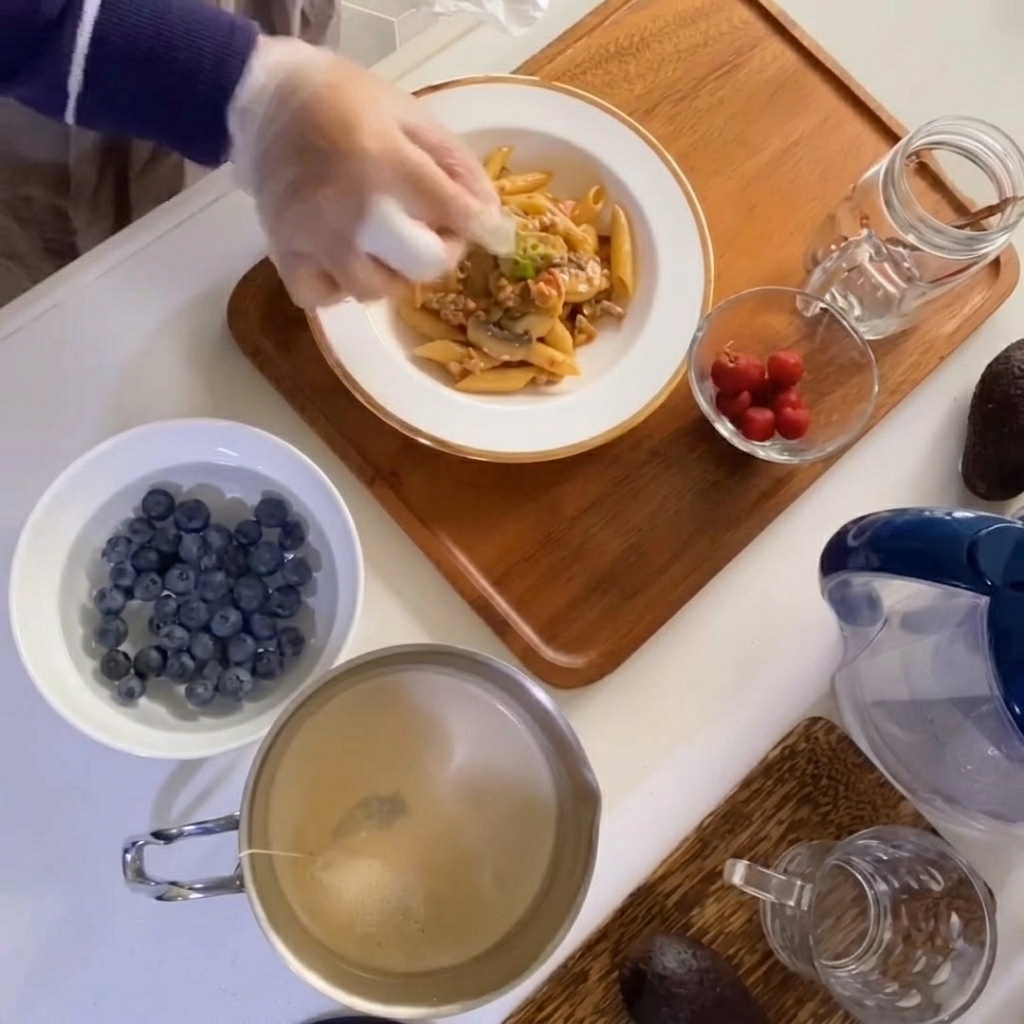 Primo piano di una mano che posiziona un rametto di timo fresco sopra il piatto di pasta.