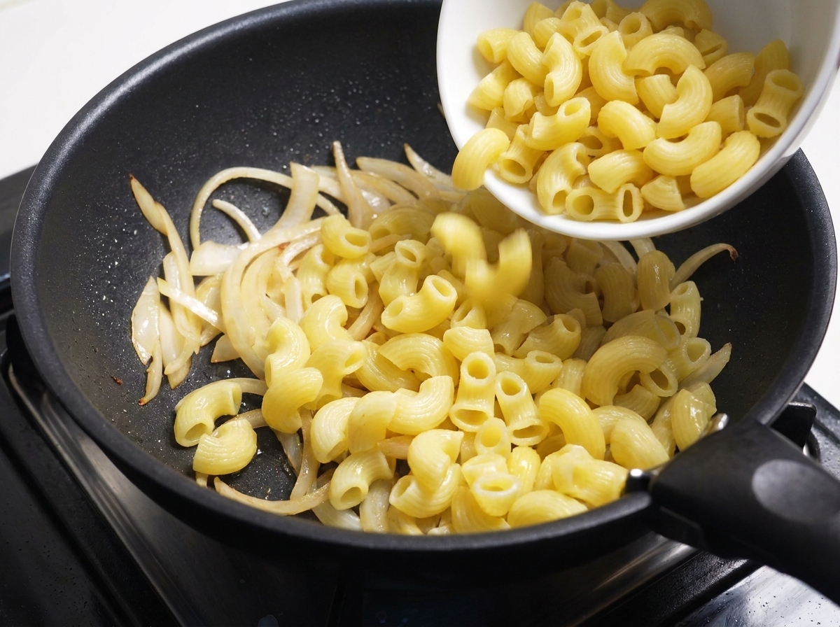 Maccheroni cotti versati da una ciotola bianca nella padella con le cipolle.