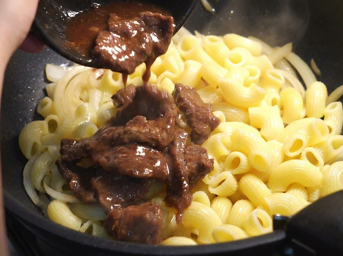Il manzo rosolato viene aggiunto nella padella con pasta e cipolle.