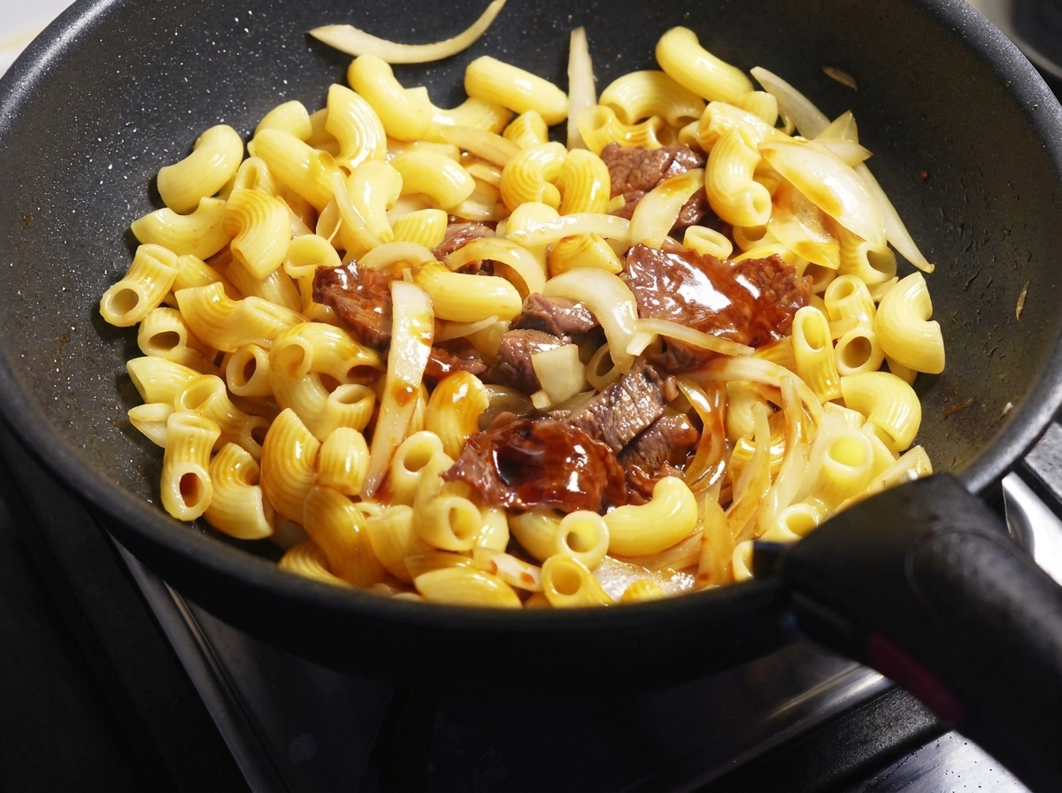 Salsa di soia scura versata sui maccheroni, il manzo e le cipolle.