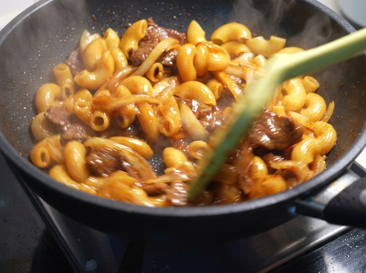 Maccheroni, manzo e cipolle saltati vigorosamente con una spatola in una padella calda.