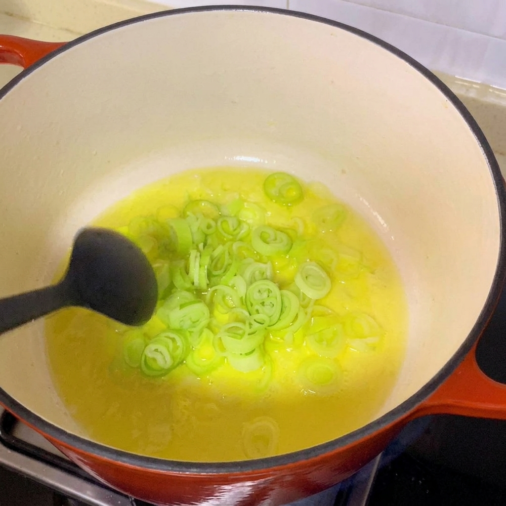 Cipollotti affettati che sfrigolano in olio caldo dentro una grande pentola rossa.