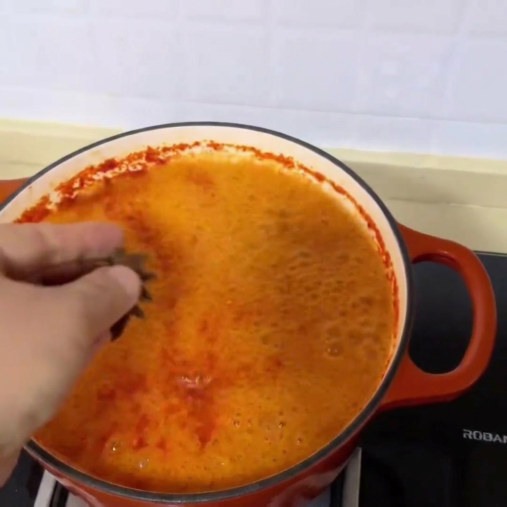 Tre anici stellati cadono nella vibrante zuppa rossa di vongole che sobbolle.