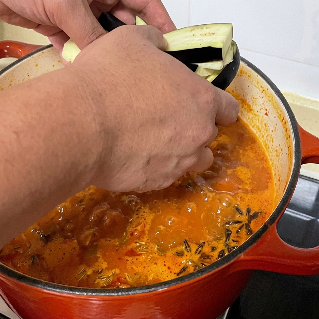 Strisce di melanzana affettate aggiunte alla pentola di zuppa piccante di vongole.