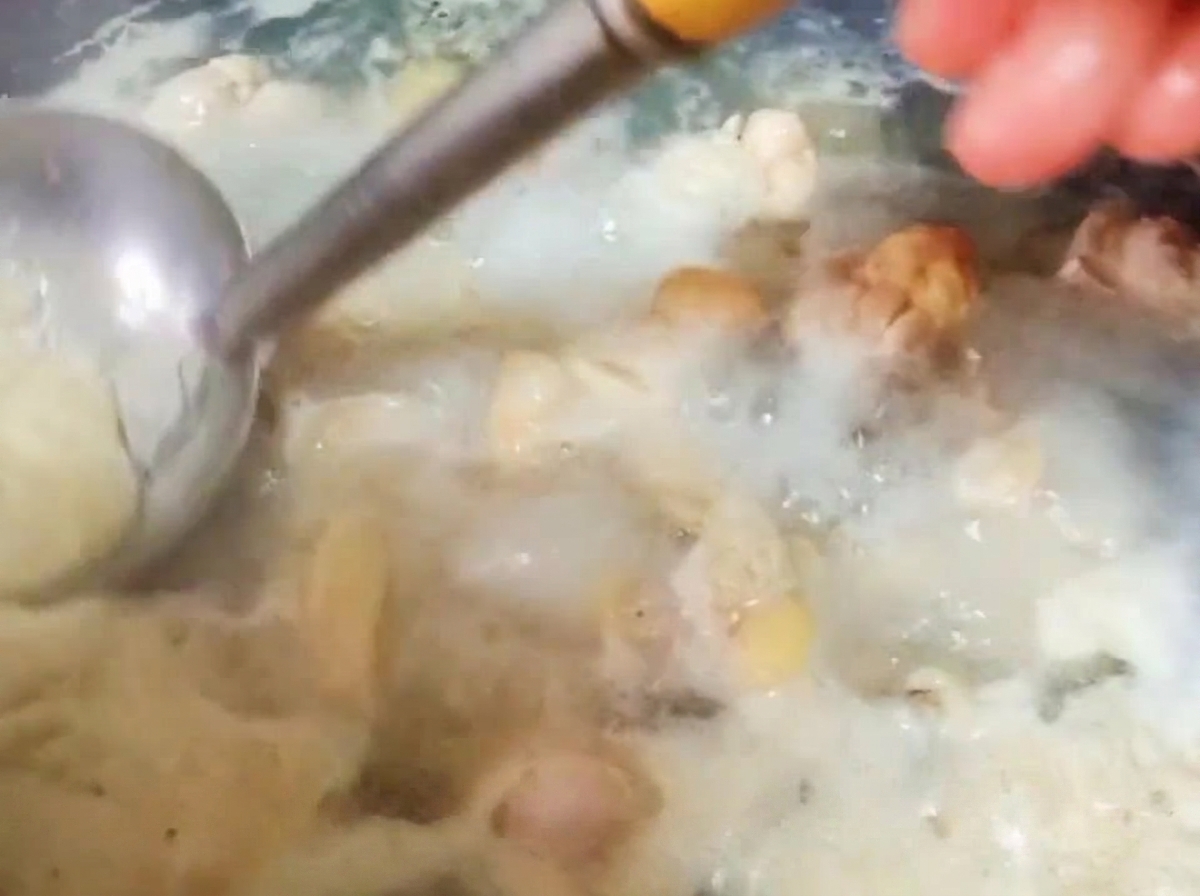 Un mestolo di metallo rimuove la schiuma densa dalla superficie dellacqua bollente con i pezzi di pollo.