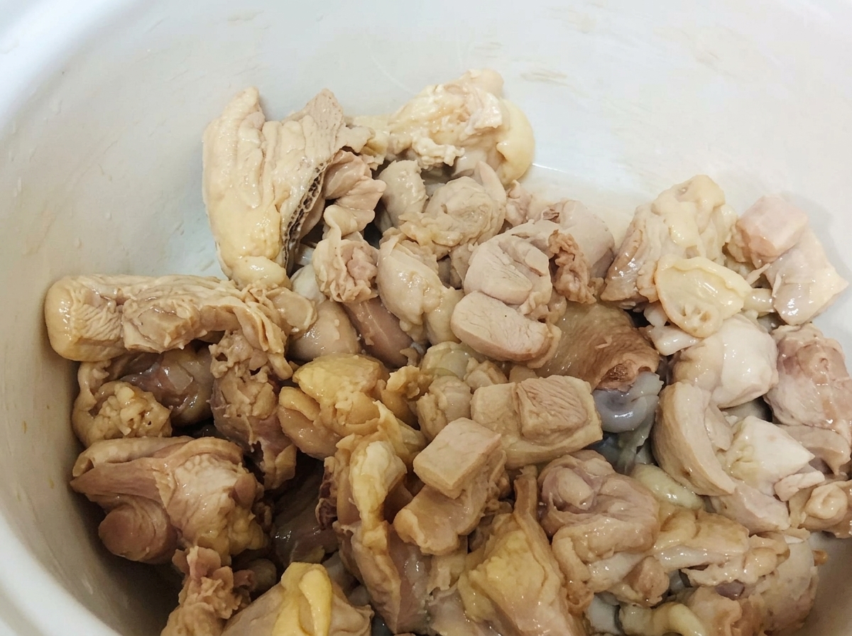 Pezzi di pollo sbollentati allinterno di una pentola di ceramica bianca.