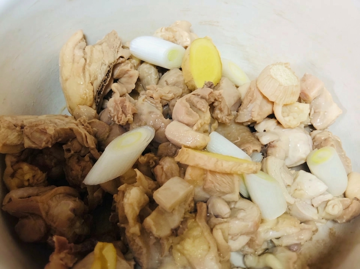Pezzi di pollo in una pentola di terracotta conditi con cipollotti, zenzero e condimenti liquidi.