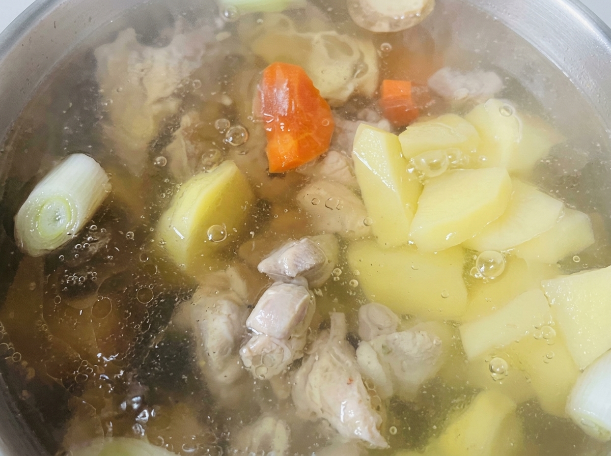 Pezzi di carote e patate che cuociono in un brodo chiaro insieme ai pezzi di pollo.