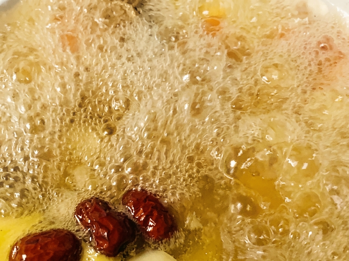 Datteri rossi e condimenti aggiunti a una pentola di zuppa di pollo che bolle.