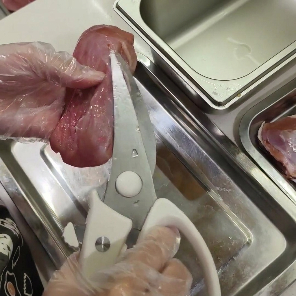 Mani con guanti tengono la carne danatra cruda mentre usano forbici da cucina per eliminare piccoli pezzi di grasso bianco.
