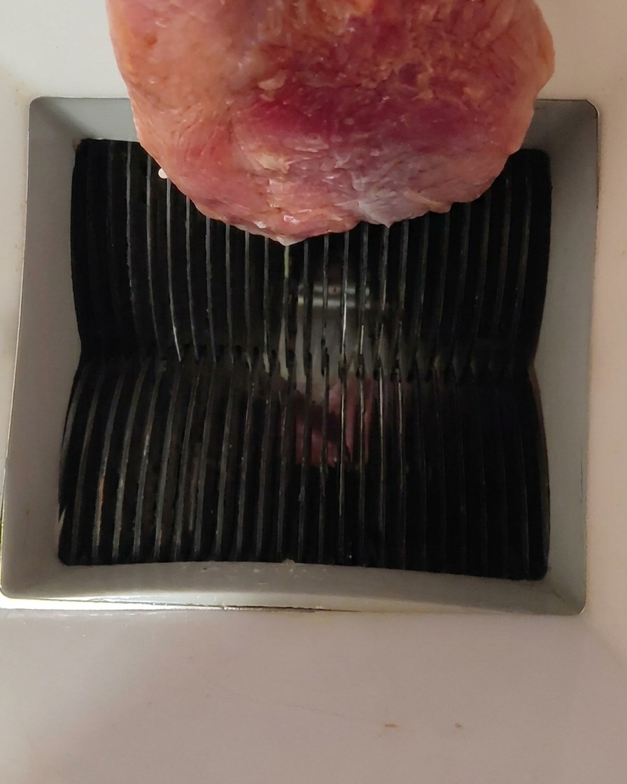 Un pezzo di carne danatra cruda inserito nella parte superiore di unaffettatrice.