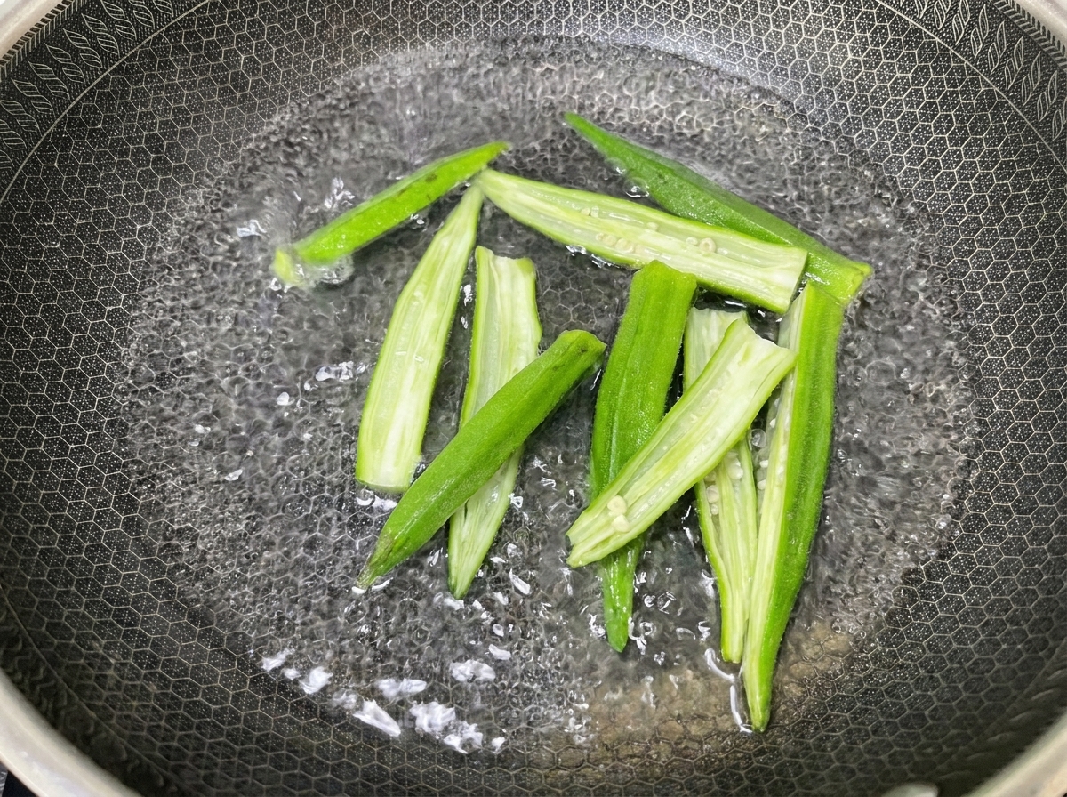 Metà di okra svuotate mentre vengono sbollentate in una pentola di metallo testurizzata piena di acqua bollente.