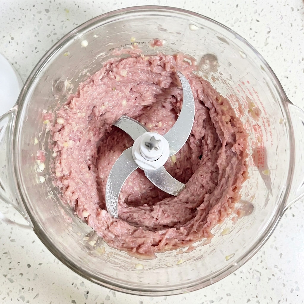 Una pasta di carne danatra cruda, finemente frullata, liscia e di colore rosa chiaro, allinterno della ciotola di vetro di un robot da cucina.
