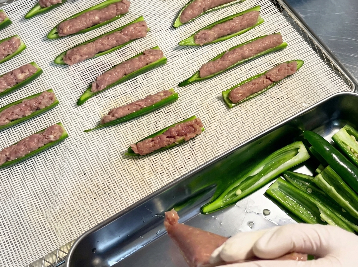 Barchette di okra riempite e disposte ordinatamente in file su un vassoio a rete in plastica per essiccatore.