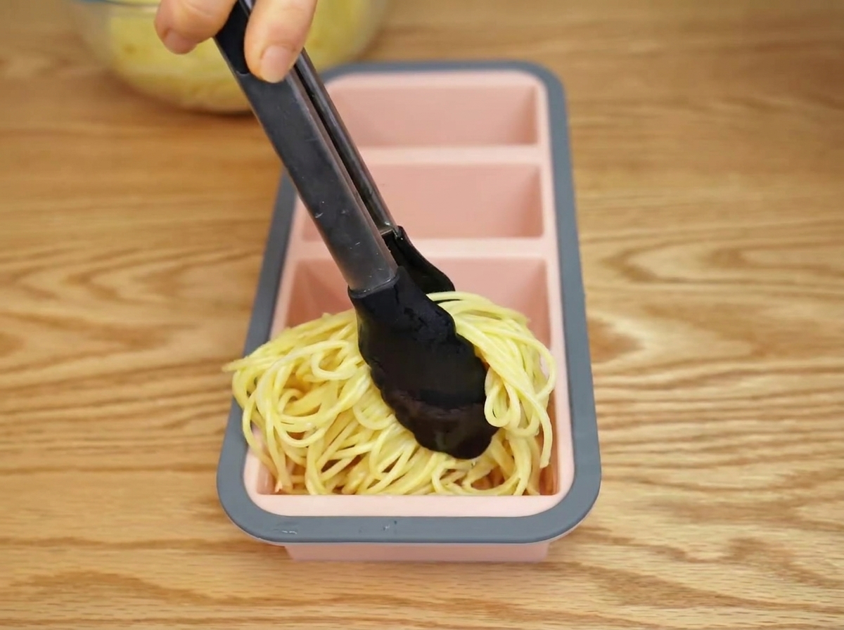 Spaghetti cotti posizionati in uno stampo di silicone con delle pinze.