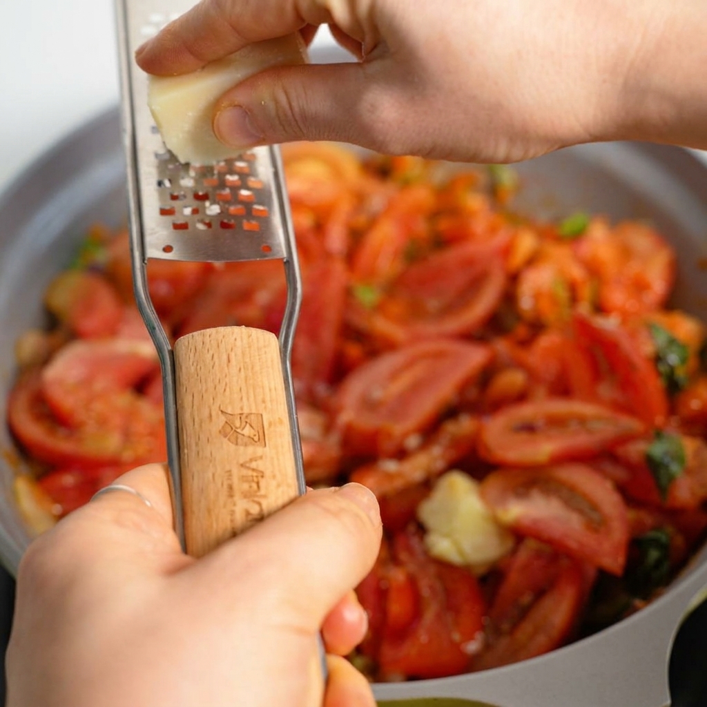 Parmigiano fresco grattugiato sopra un abbondante e scoppiettante ragù di carne in una padella.