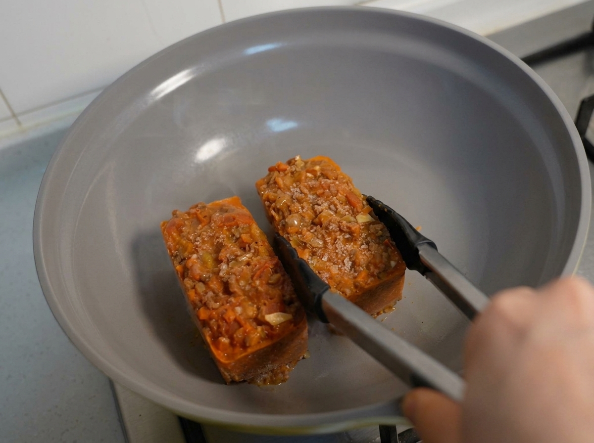 Blocchi congelati di pasta e ragù riscaldati in una padella con delle pinze.
