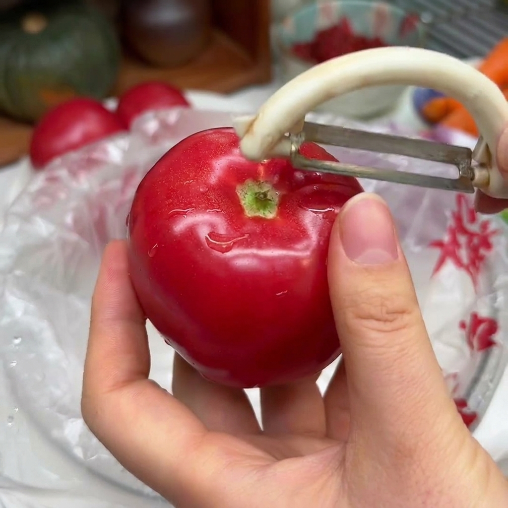 Mani che tengono un pomodoro rosso vivo mentre usano un pelapatate bianco per togliere la buccia.