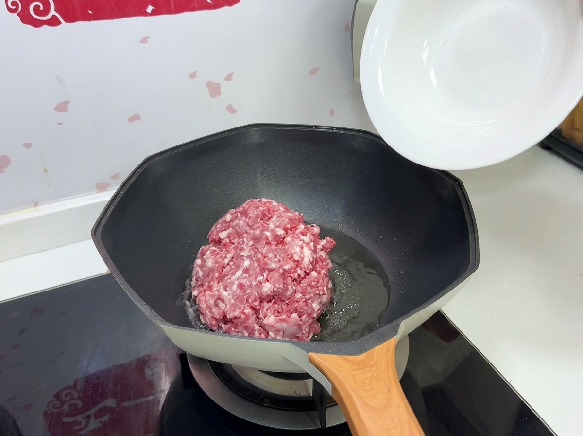 Macinato di maiale crudo versato da una ciotola bianca in una padella calda con olio.