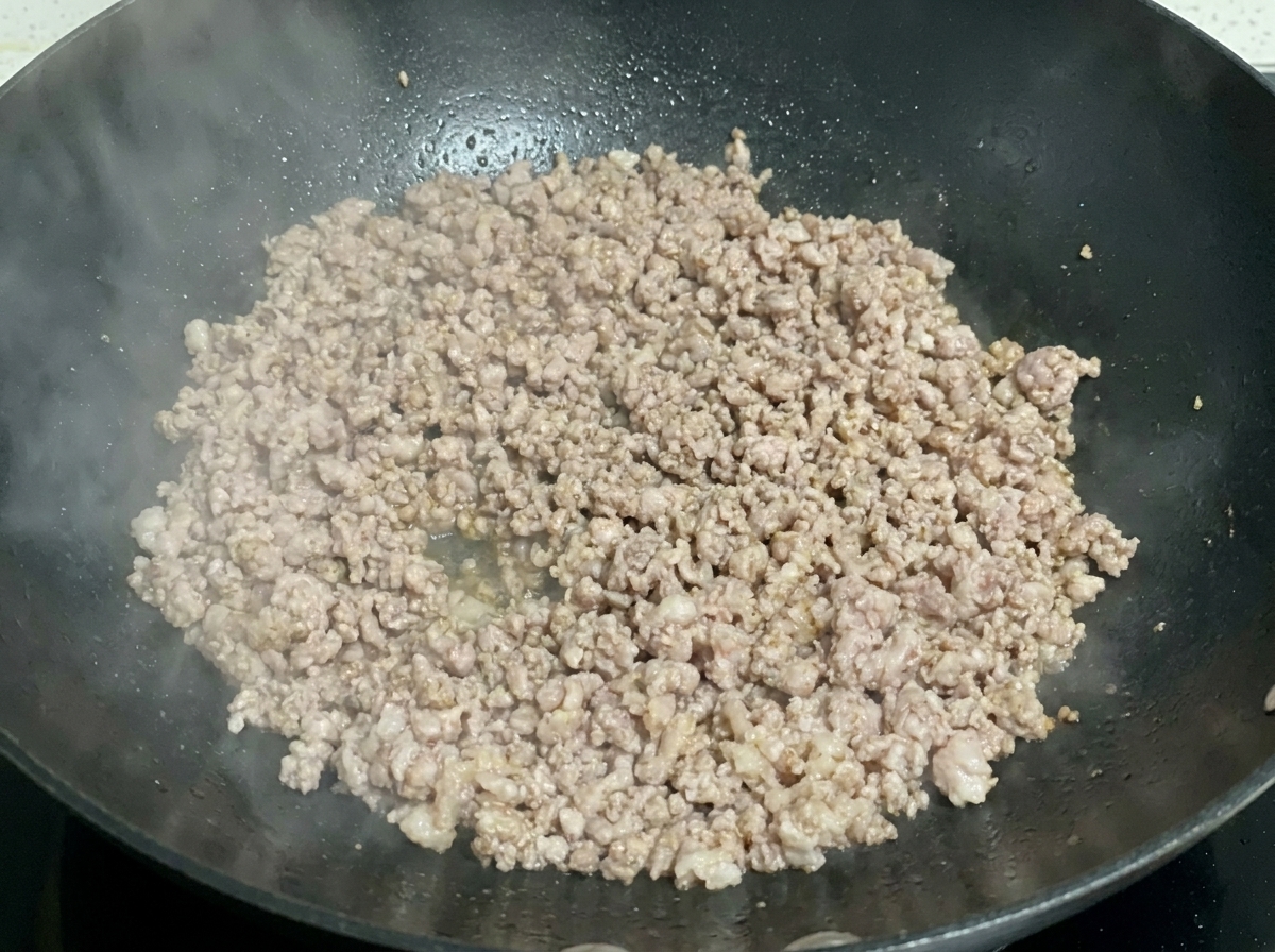 Carne macinata cotta e leggermente dorata che sfrigola in un wok scuro.