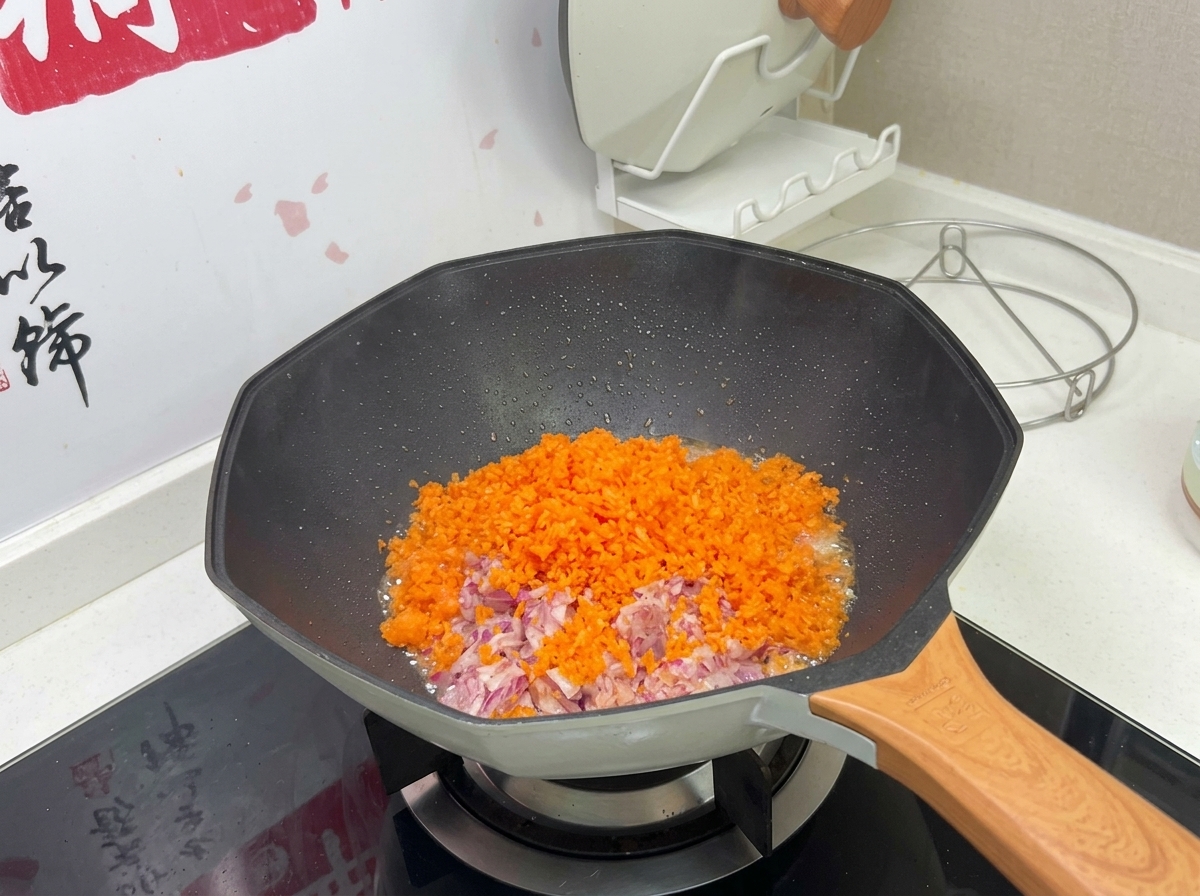 Un trito colorato di carote arancioni e cipolle rosse in cottura in un wok caldo.