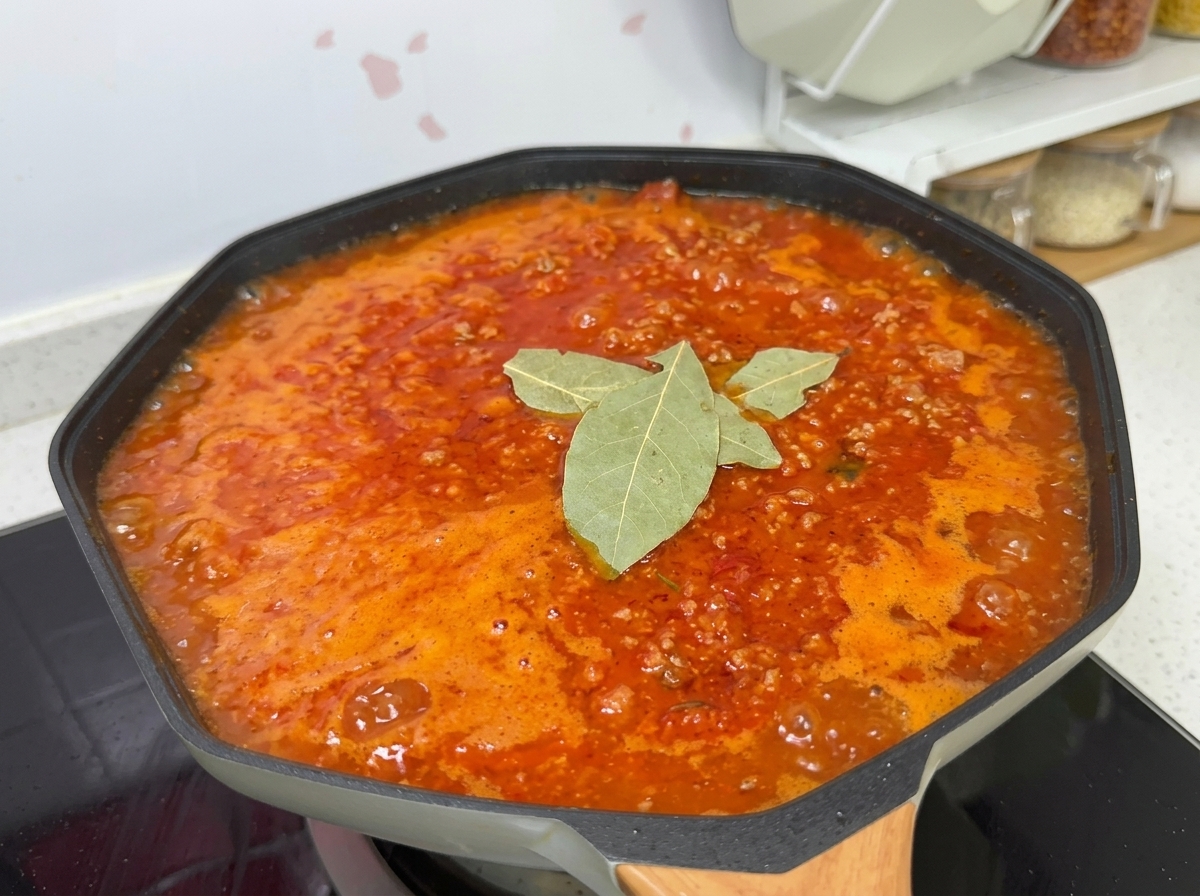 Un ragù in ebollizione in un wok, condito con sale, zucchero, alloro e pepe nero.