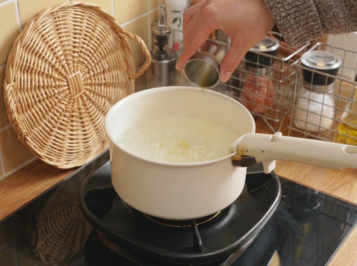 Olio versato da un misurino metallico in una pentola di acqua bollente.