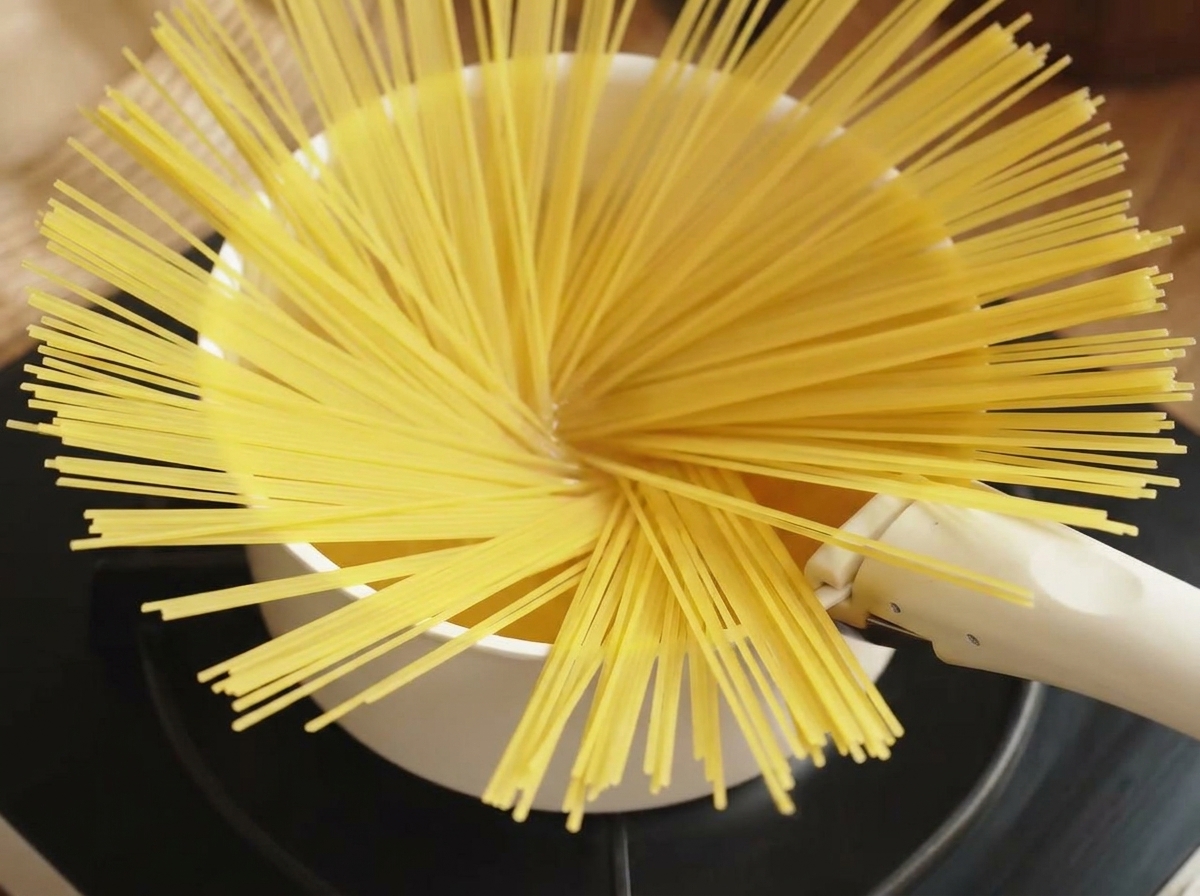 Un mazzetto di spaghetti secchi aggiunto a una pentola di acqua bollente.