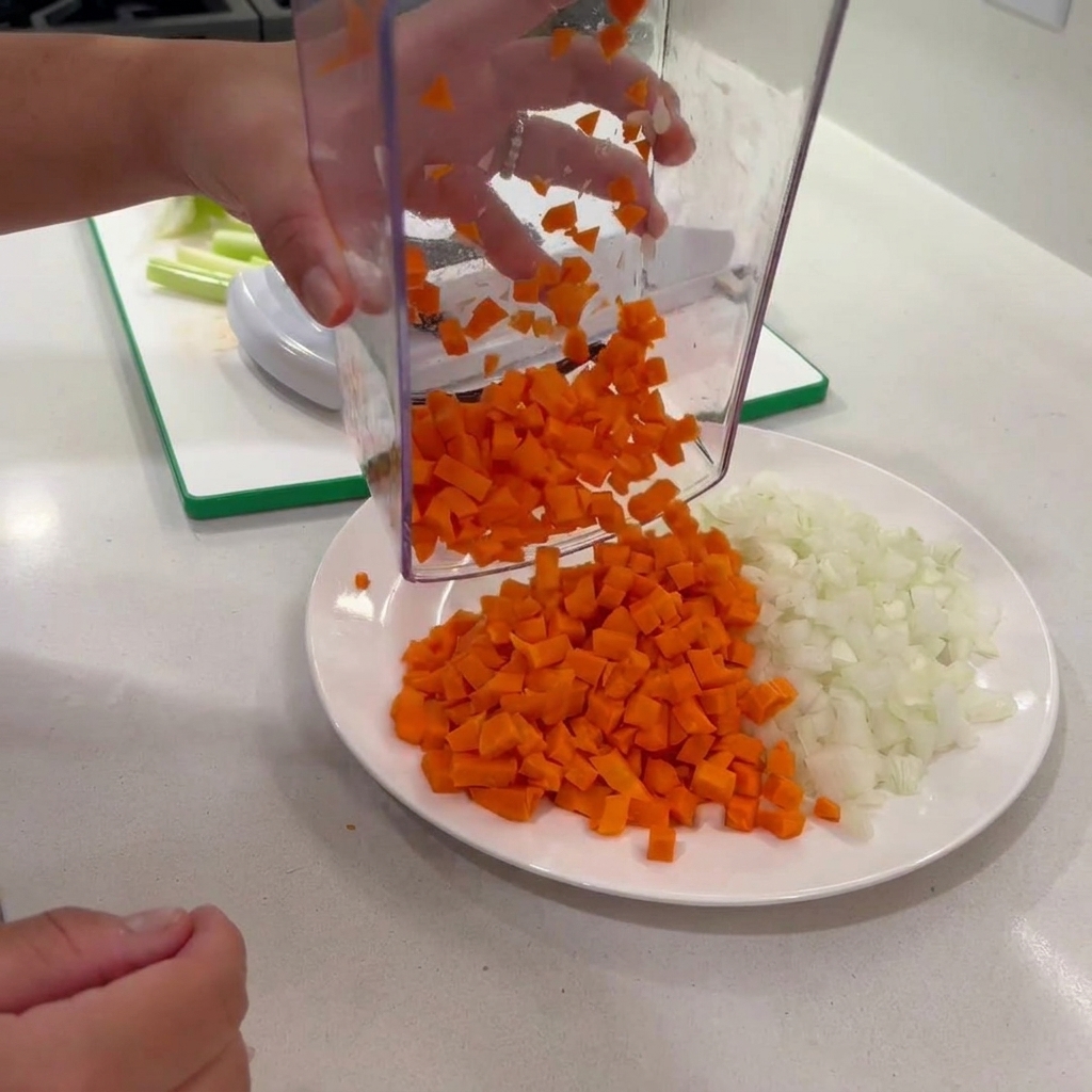 Carote a cubetti versate da un tritatutto su un piatto con cipolle.