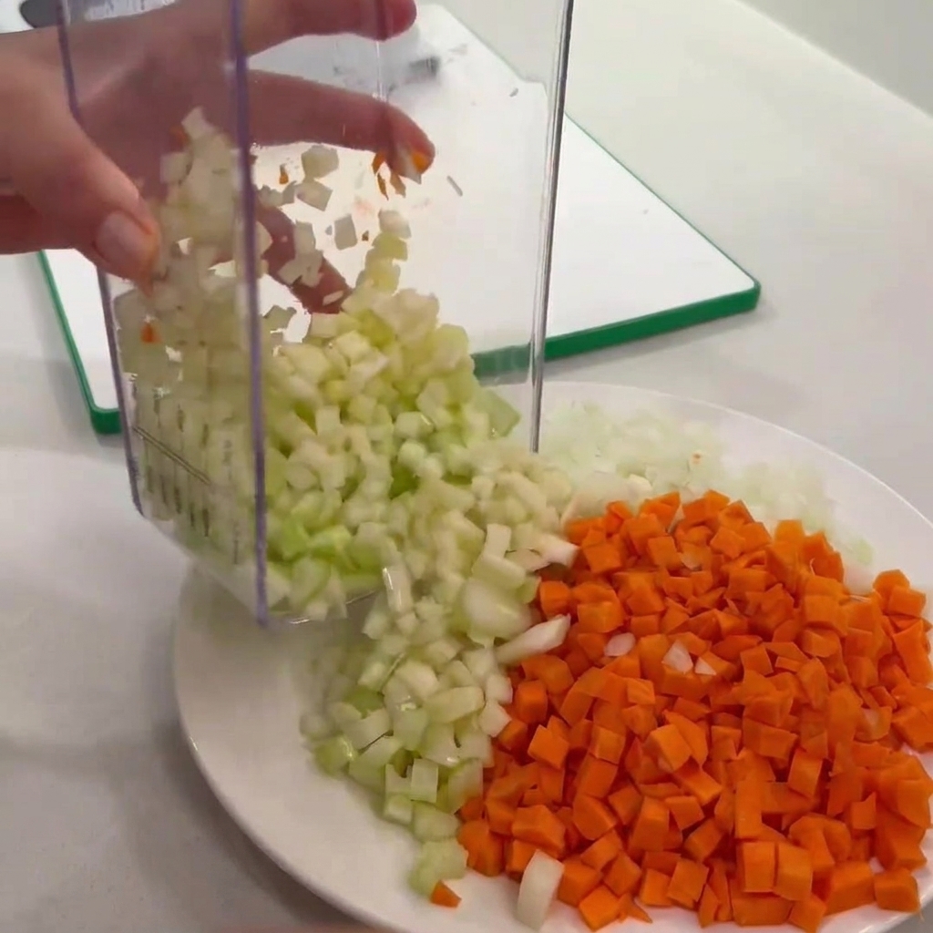 Sedano a cubetti versato da un tritatutto su un piatto con carote e cipolle.