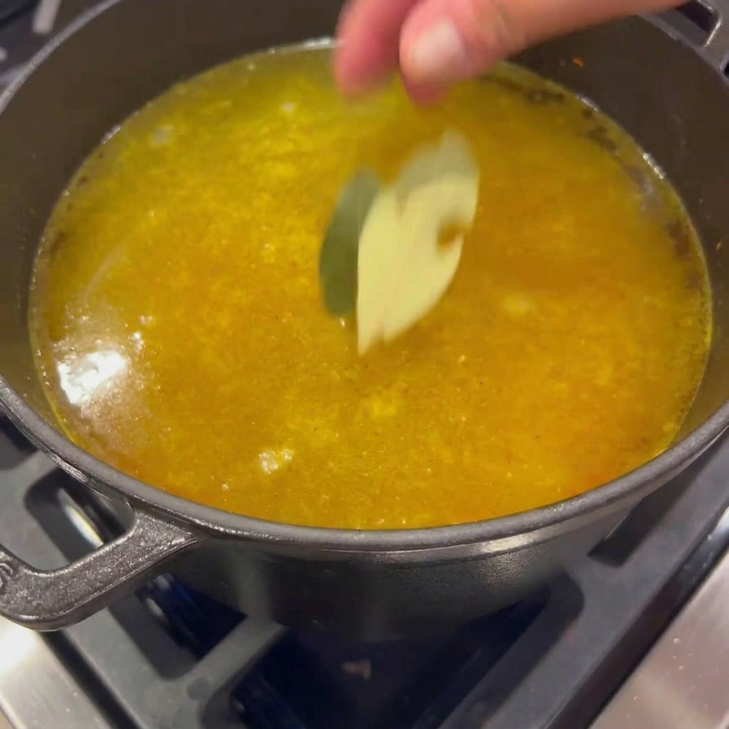 Due foglie di alloro essiccate versate in una pentola di brodo con verdure.