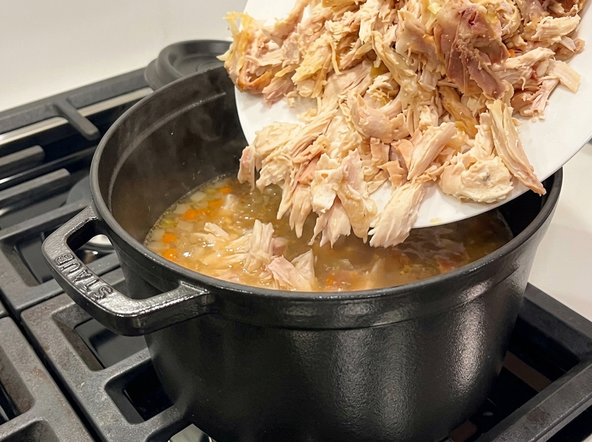 Pollo sfilacciato aggiunto da un piatto in una pentola nera di zuppa in ebollizione.