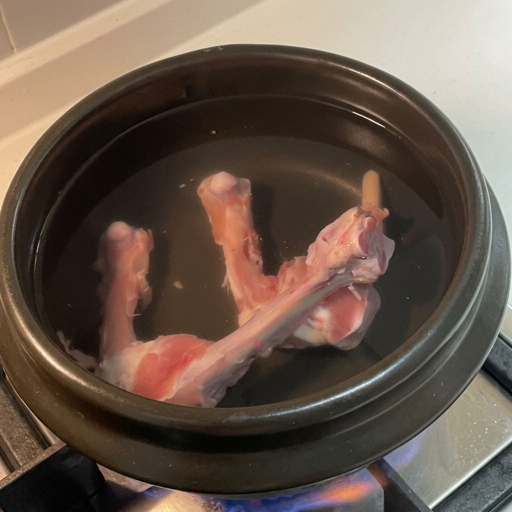 Fette di zenzero, grani di pepe bianco e una foglia di alloro galleggiano nellacqua con le ossa di pollo.