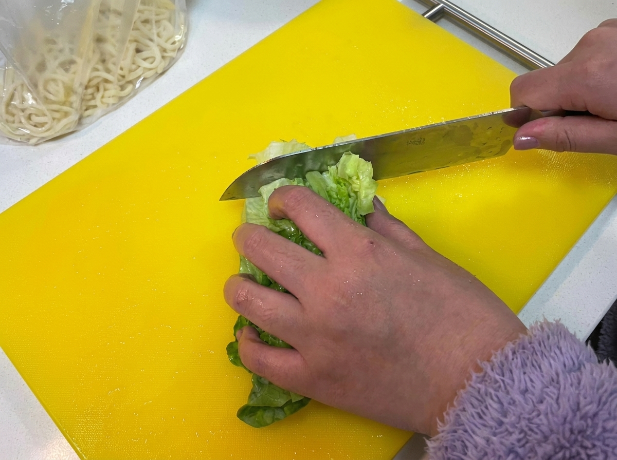 Foglie di lattuga verde fresca tritate su un tagliere giallo brillante.