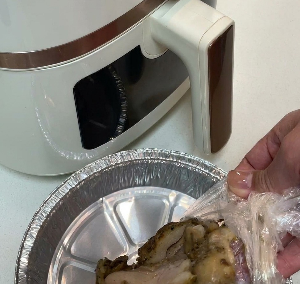 Carne di coscia di pollo pre-condita posizionata in un cestello per friggitrice ad aria foderato di alluminio.