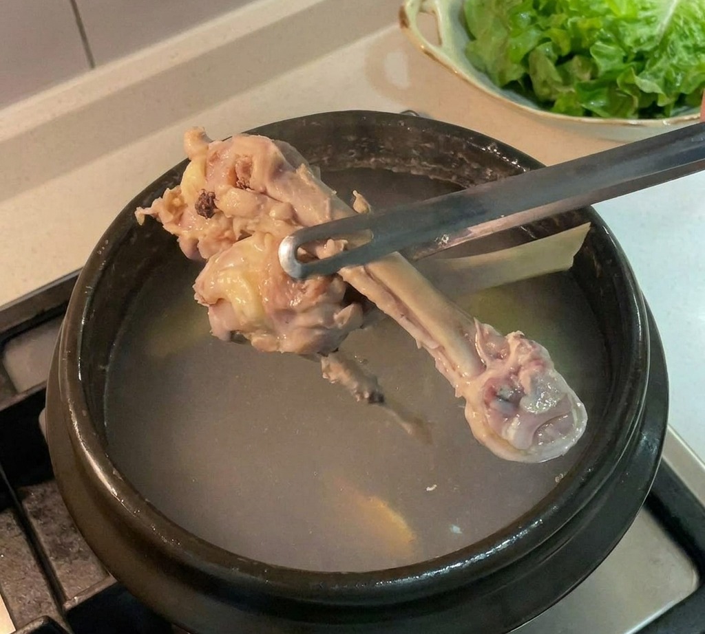 Ossa di pollo sollevate da una pentola scura di brodo utilizzando pinze di metallo.