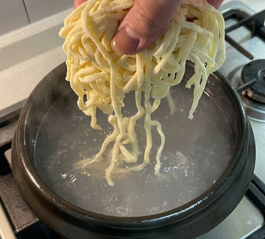 Noodles freschi calati in una pentola di brodo di pollo in ebollizione.
