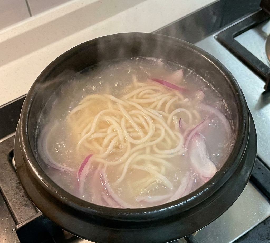 Cipolle rosse a fette che sobbollono in una pentola di brodo con noodles.