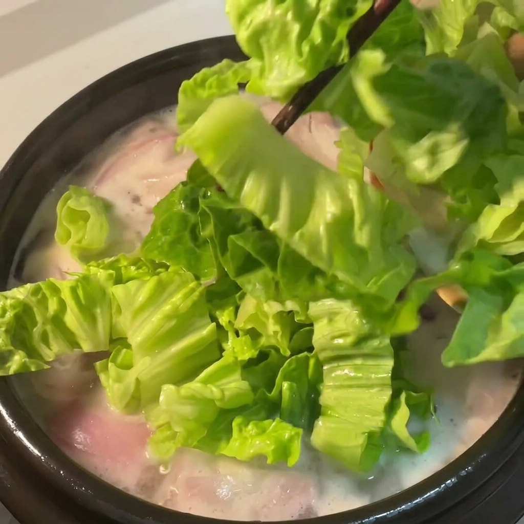 Lattuga verde fresca fatta cadere nel brodo di pollo che sobbolle con le cipolle rosse.