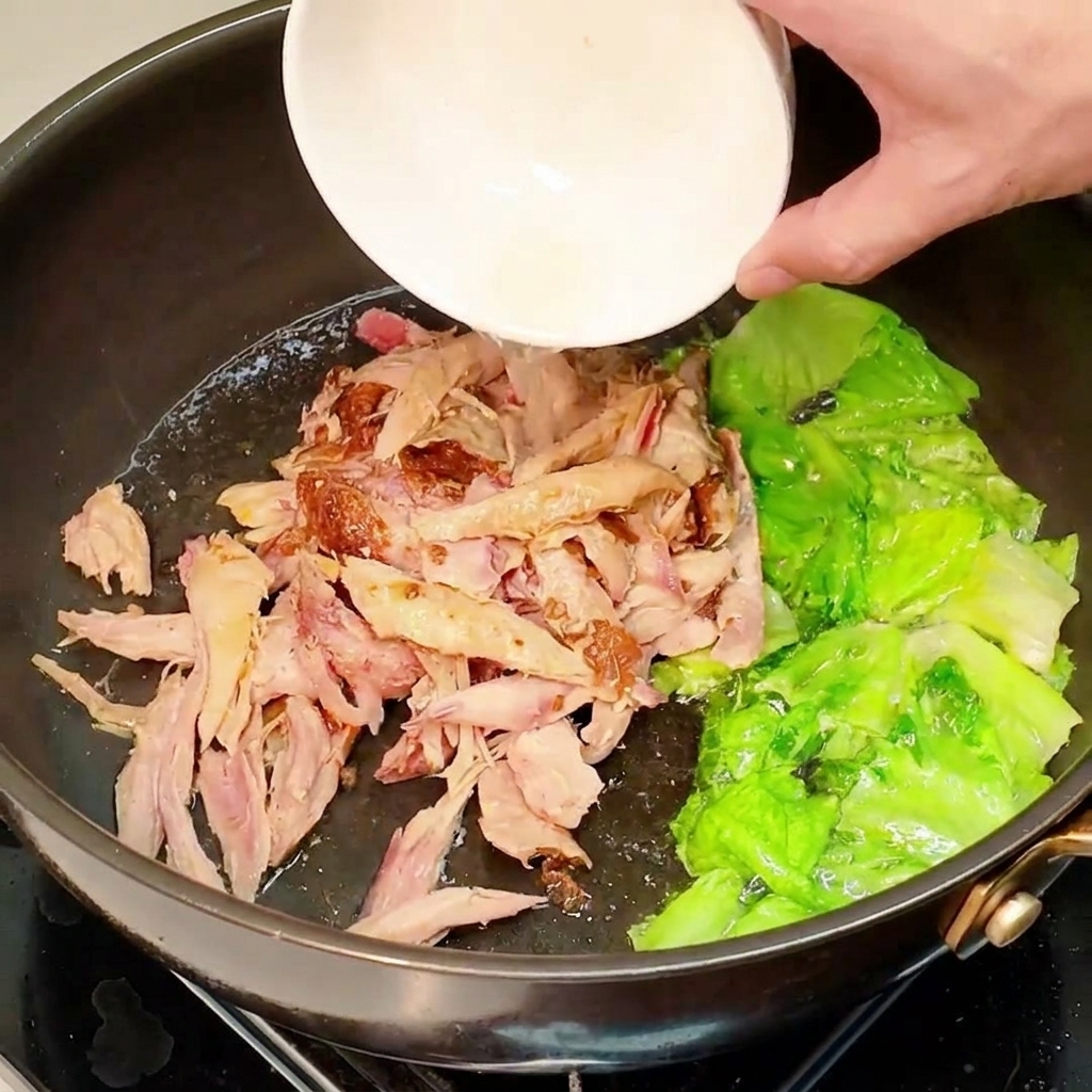 Pollo sfilacciato precotto aggiunto in padella con la lattuga.