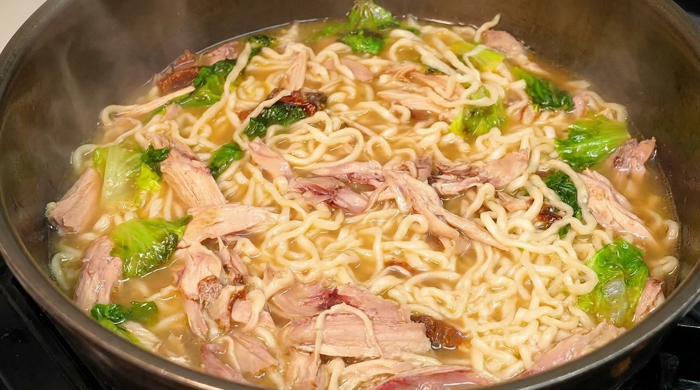 Una fumante ciotola di zuppa di noodles con pollo al pepe sfilacciato, verdure e noodles ondulati.