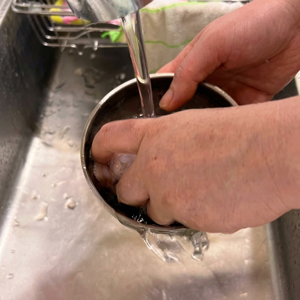 Ali di pollo fresche lavate in una ciotola di acciaio inossidabile sotto il rubinetto della cucina.